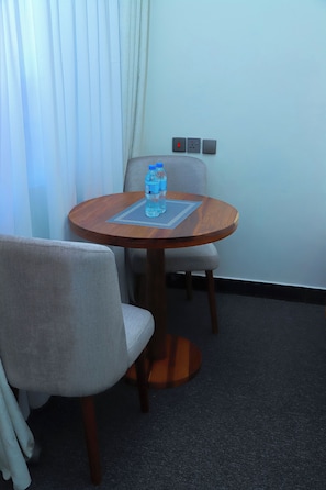 A small round table with two chairs, a water bottle, and a power outlet on the wall. - Ken Homestay (Arusha)