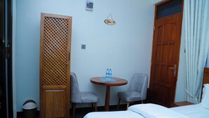 Habitación de hotel con cama, dos sillas, una mesita con botellas de agua, un armario de madera y una puerta.