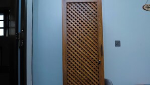Una habitación con una puerta de madera, una silla gris, una mesita y un cesto de basura.