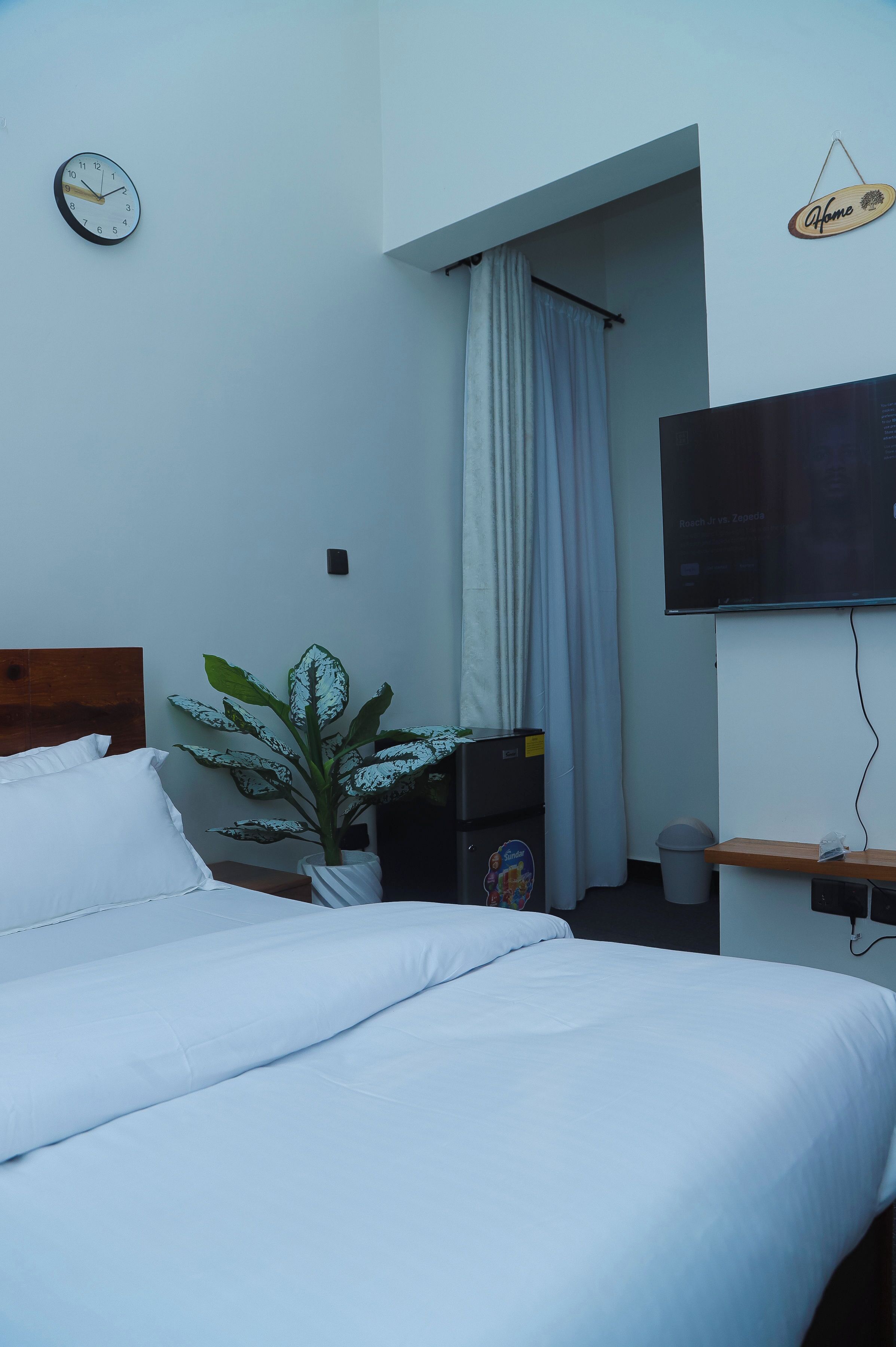 Una habitación de hotel con una cama, una planta, un televisor y un cartel que dice 'Home'.