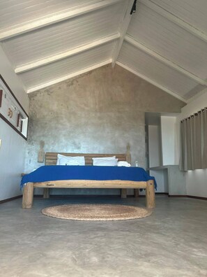A bedroom with a sloped ceiling, a wooden bed with a blue bedspread, a round rug, and a wall-mounted cabinet.