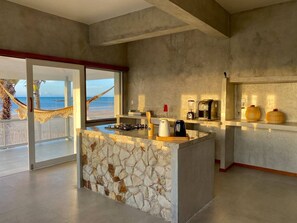 A modern kitchen with a stone island, a view of the beach, and a hammock outside.