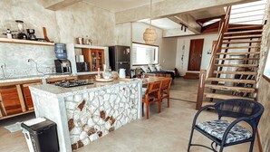 Una cocina amplia con una isla central, sillas de madera, una mesa de comedor y una escalera que lleva a un nivel superior.