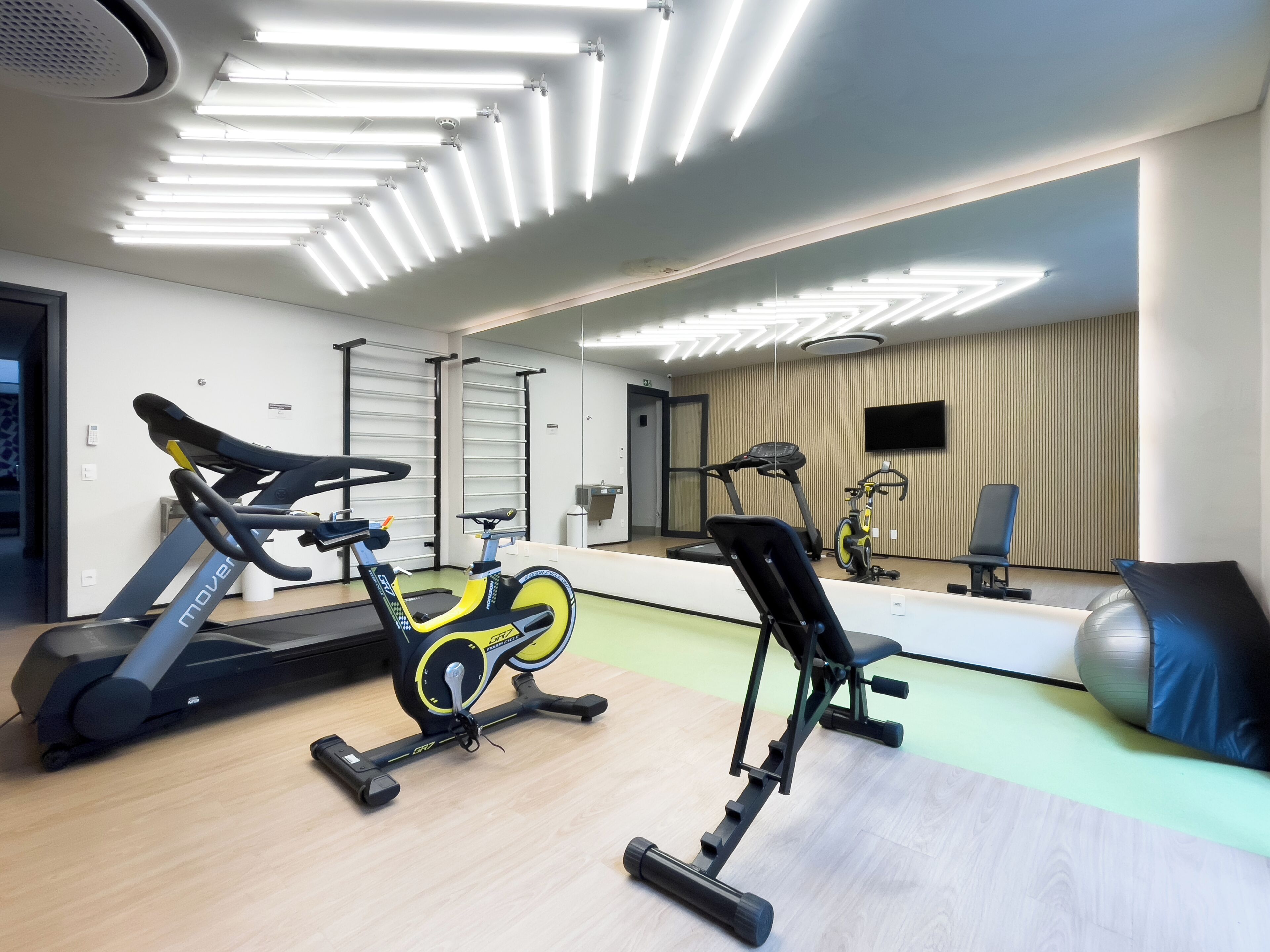 Een sportschool met trainingsapparatuur, een spiegel en een televisie.