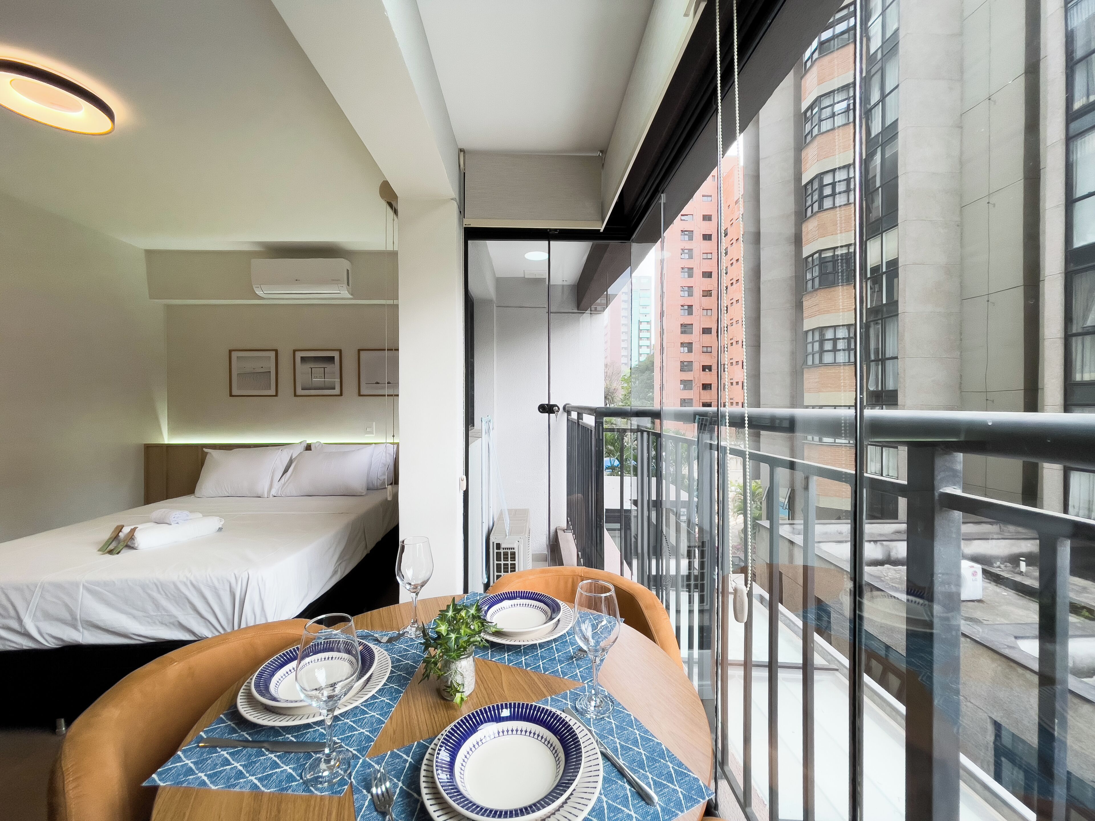 A hotel room with a balcony, a bed, a dining table set with plates and glasses, and a view of the cityscape.
