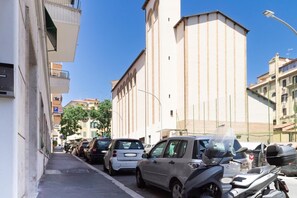 Eine schmale Stadtstraße mit parkenden Autos und einem Gebäude mit vertikalen Fenstern.