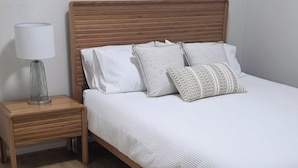 Ein Schlafzimmer mit einem Holzbett, weißer Bettwäsche, einem Nachttisch mit Lampe und Holzboden.