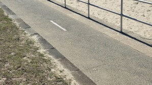 Eine Küstenstraße mit Metallgeländer, die zu einem Sandstrand führt.