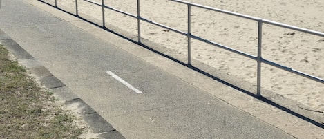 A coastal road with a metal railing, leading to a sandy beach.
