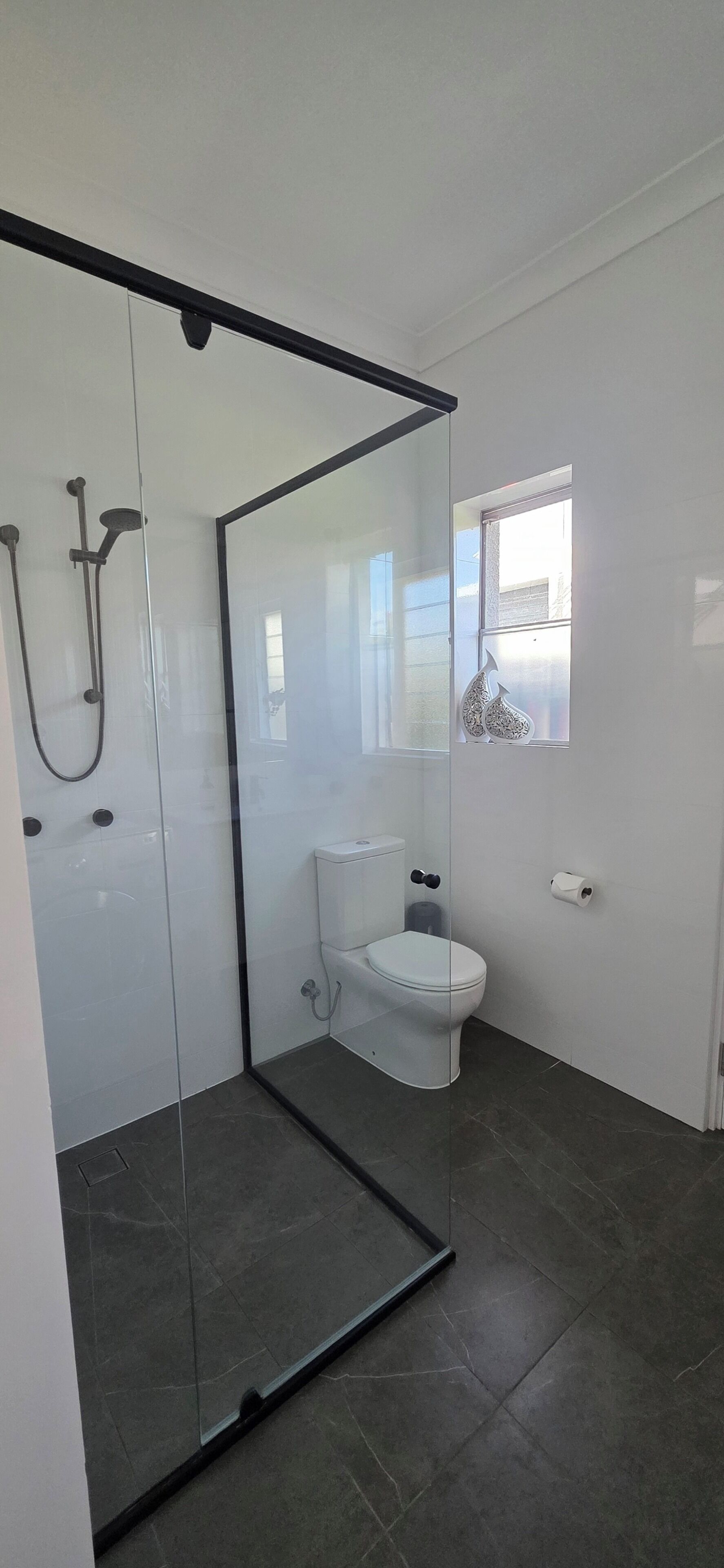 A modern bathroom with a glass-enclosed shower, a toilet, and a small window.