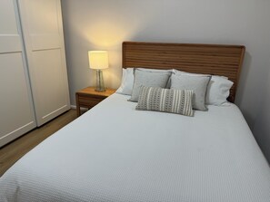 A neatly made bed with a wooden headboard, a bedside lamp, and two patterned pillows.