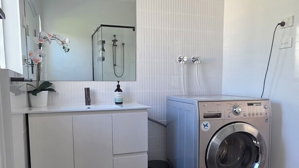 Ein modernes Badezimmer mit weißem Waschtisch, einem Spiegel, einem Waschbecken, einer Toilette und einer Waschmaschine.