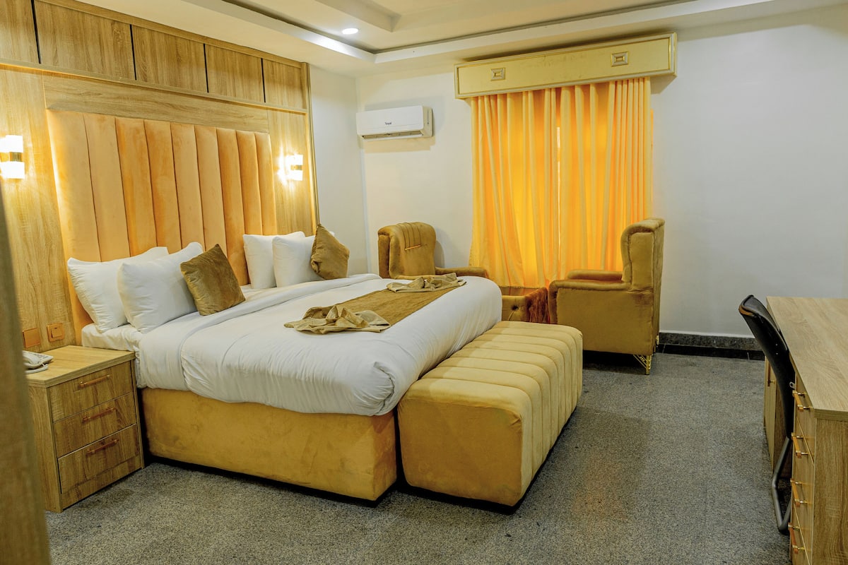 Quarto de hotel com uma cama grande, uma escrivaninha, uma cadeira e um ar condicionado.