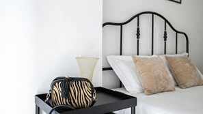 En säng med vita och beige kuddar, en svart metallgavel och en väska med zebrasträck på ett svart brickbord.