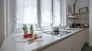 Una cocina moderna con cubierta blanca, un lavamanos, una estufa y un ventanal con cortinas translúcidas.