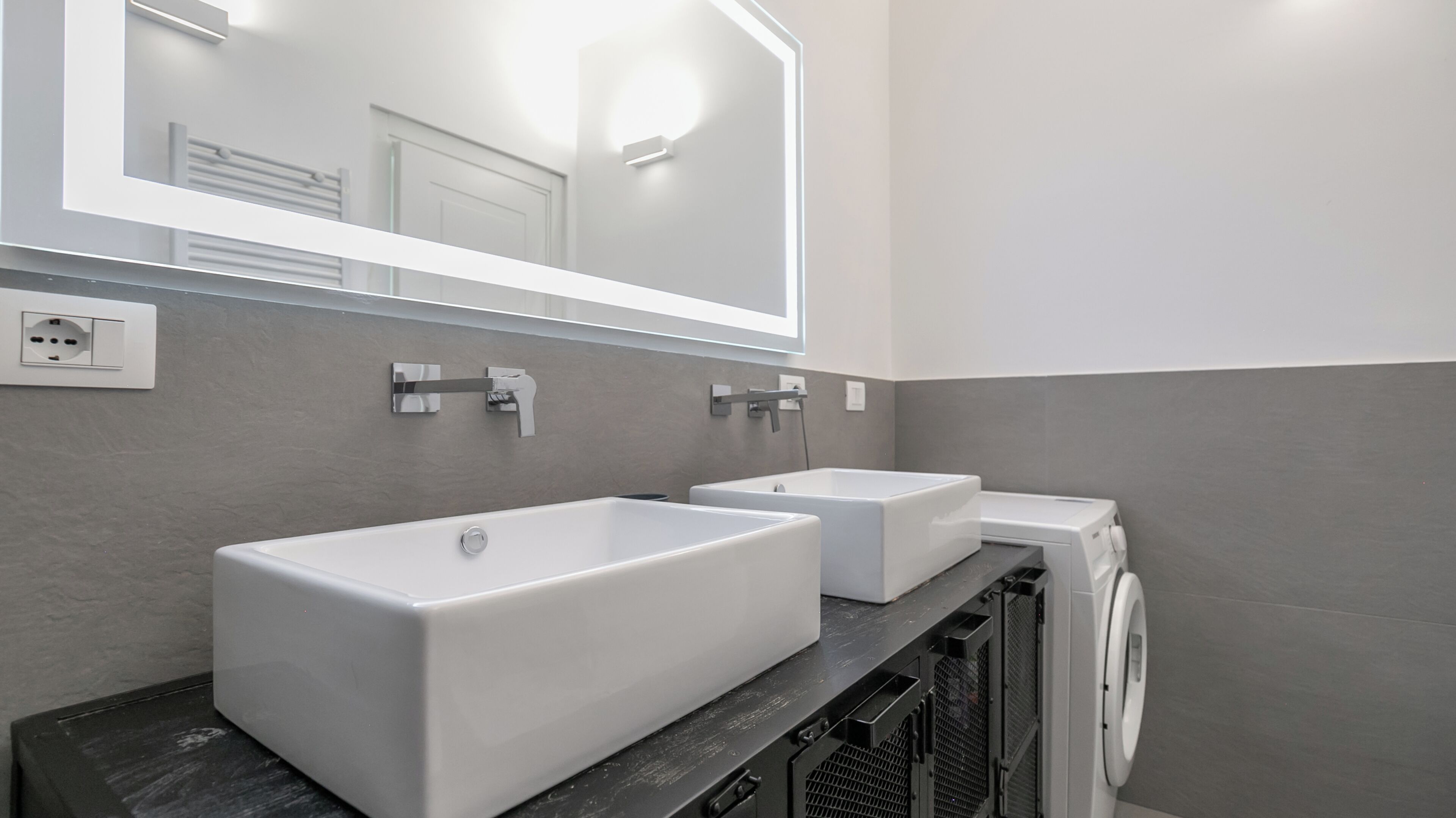 A modern bathroom with two sinks, a mirror, and a washing machine.