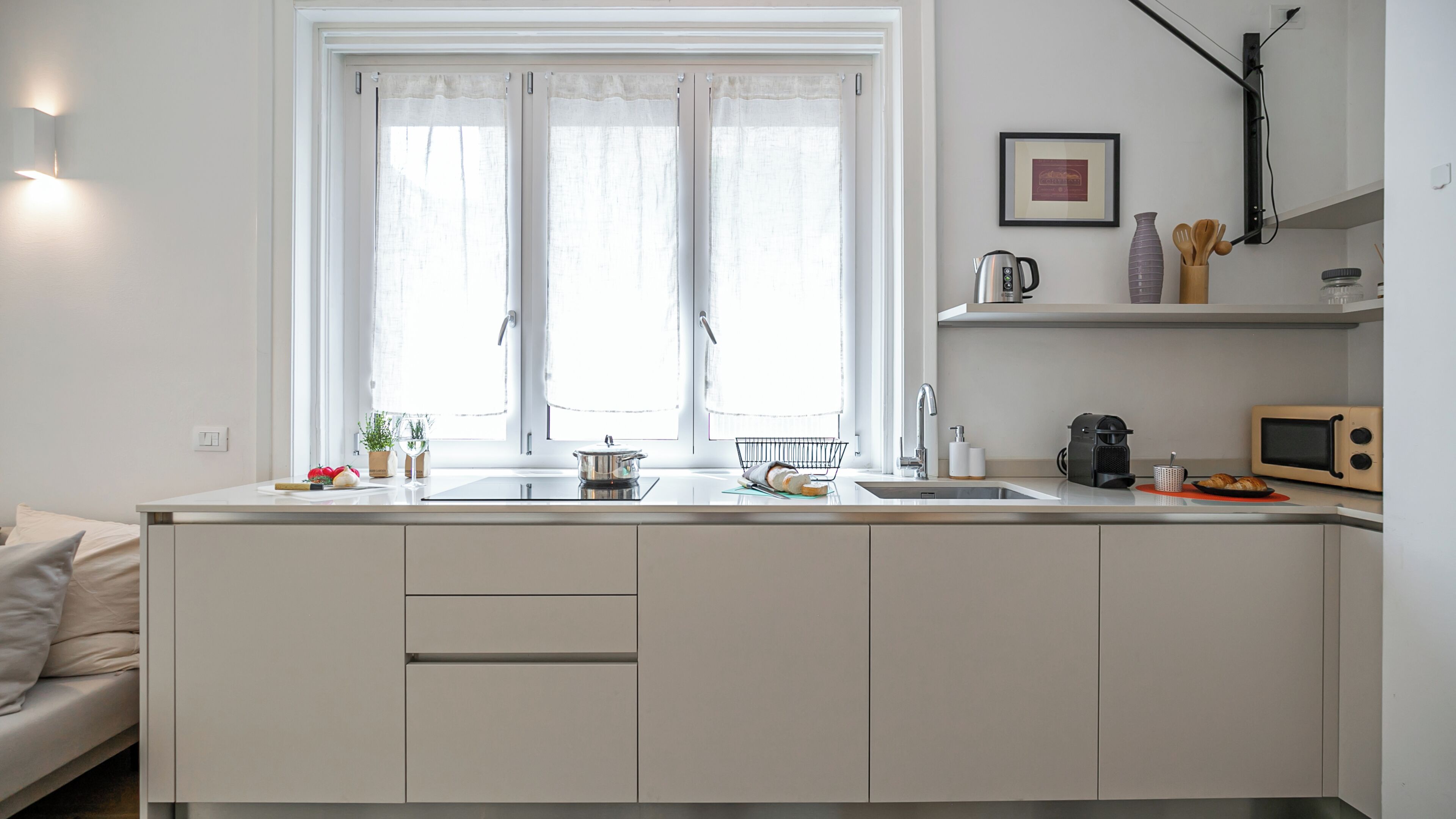 Une cuisine moderne dotée d’une grande fenêtre, d’un évier, d’un four à micro-ondes et d’une bouilloire.