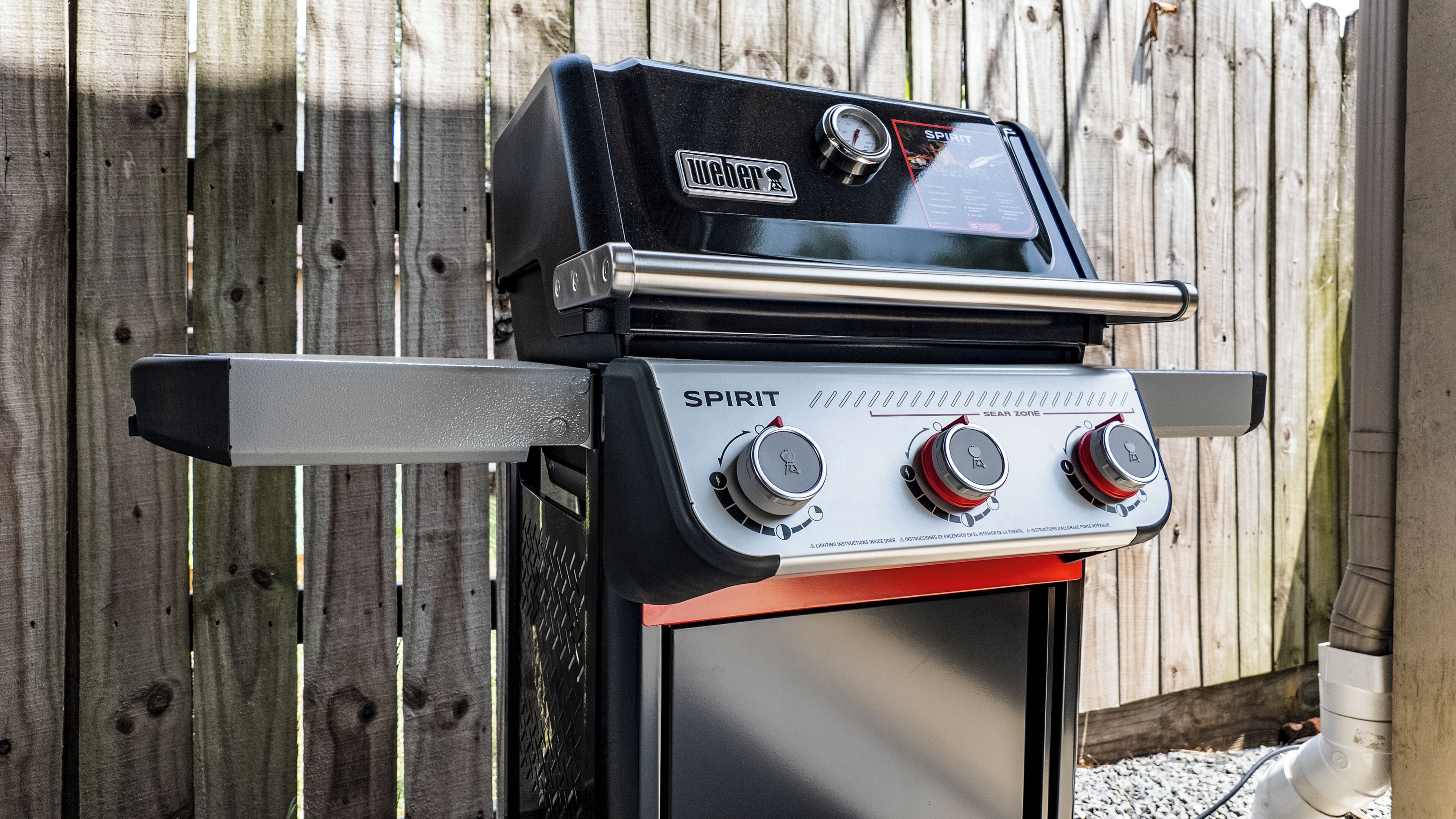 A Weber Spirit gas grill with a digital thermometer and a sear zone indicator, mounted on a metal stand.