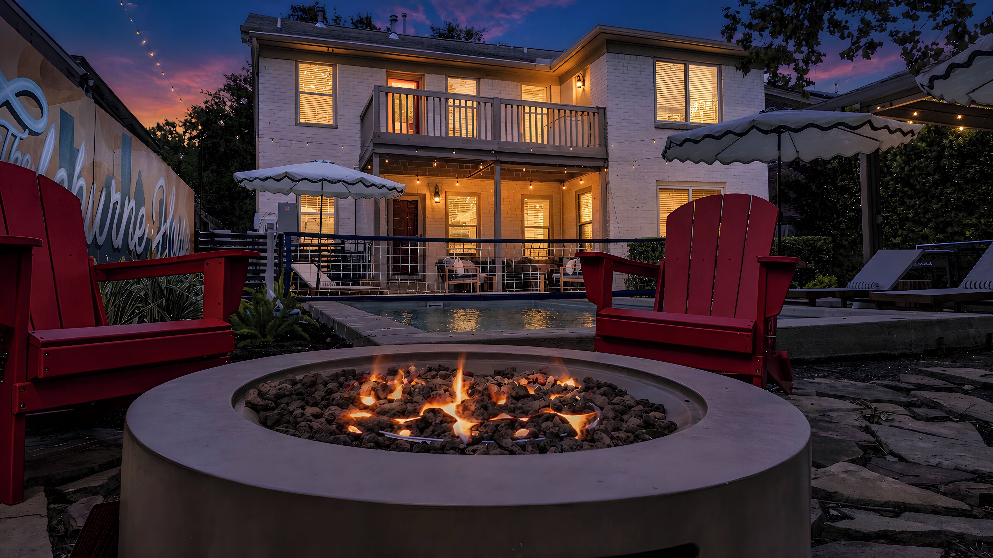 A poolside area with a fire pit, outdoor seating, and a building with a balcony.