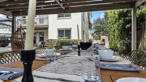 An outdoor dining area with tables set for two, chairs, and a hanging chair. - Posh Retreat· Heated Pool&HotTub/Game Room/Sleep16 (Houston)