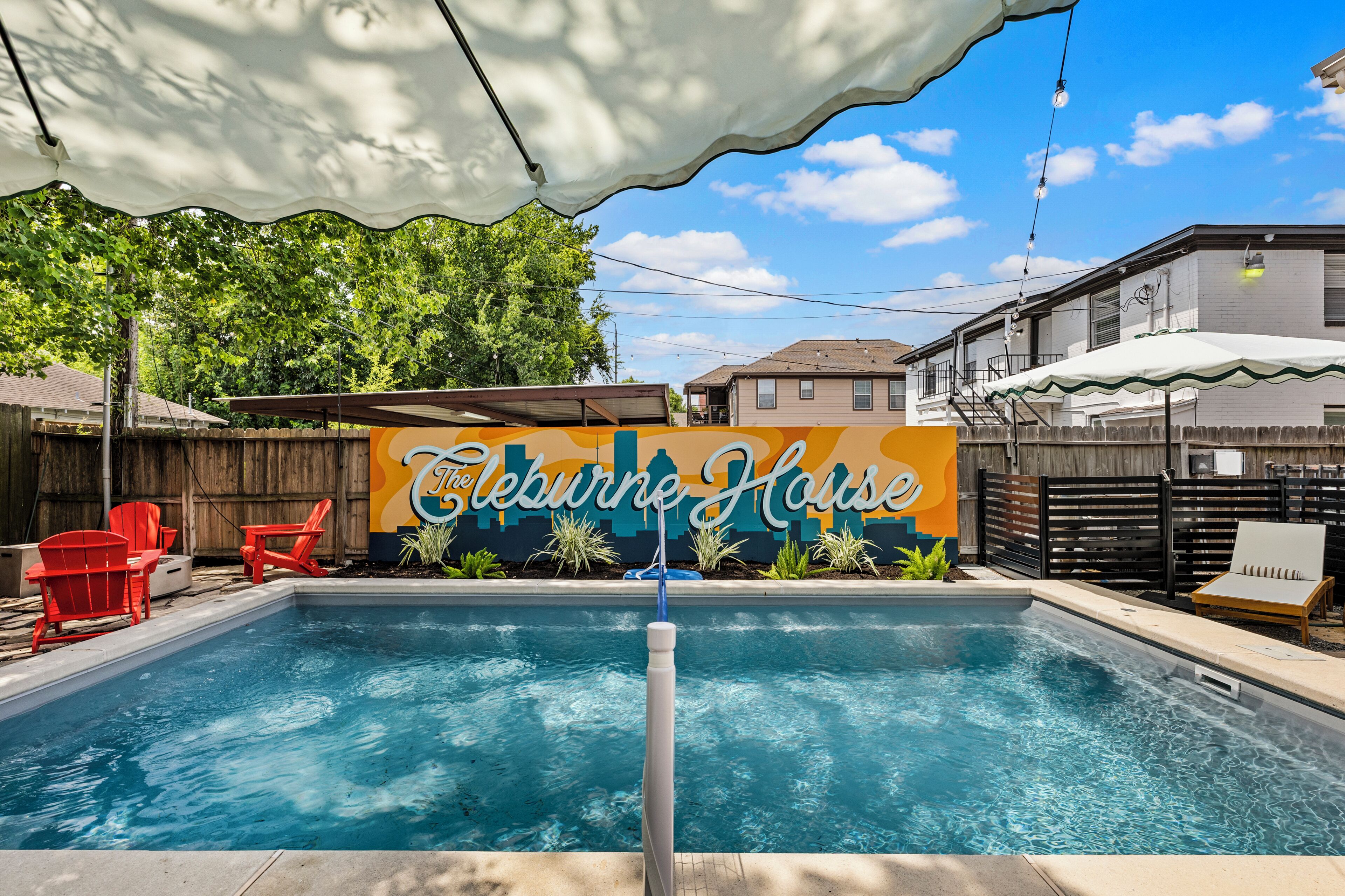 Ein Swimmingpool mit einem Schild, auf dem 'The Leburn House' steht, und roten Stühlen darum.