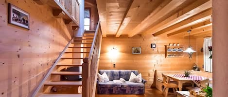 Un interior de madera con una escalera, un sofá, una mesa de comedor y una zona de cocina.