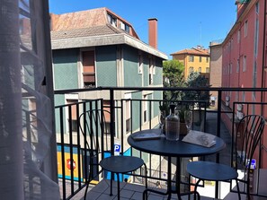 Ein Balkon mit zwei runden Tischen und Stühlen, mit Blick auf eine Straße mit Gebäuden und einem Parkschild.