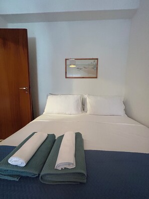 Ein Hotelzimmer mit einem Bett, zwei Kissen, einem gefalteten Handtuch, einer Holztür und einem gerahmten Bild an der Wand.
