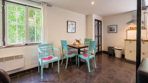 Un comedor con una mesa y sillas, una ventana con cortinas, un radiador y un armario con utensilios de cocina.