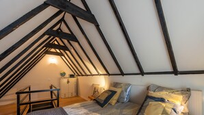 Un dormitorio con techo inclinado, una cama con ropa de cama estampada, una mesita y un armario.