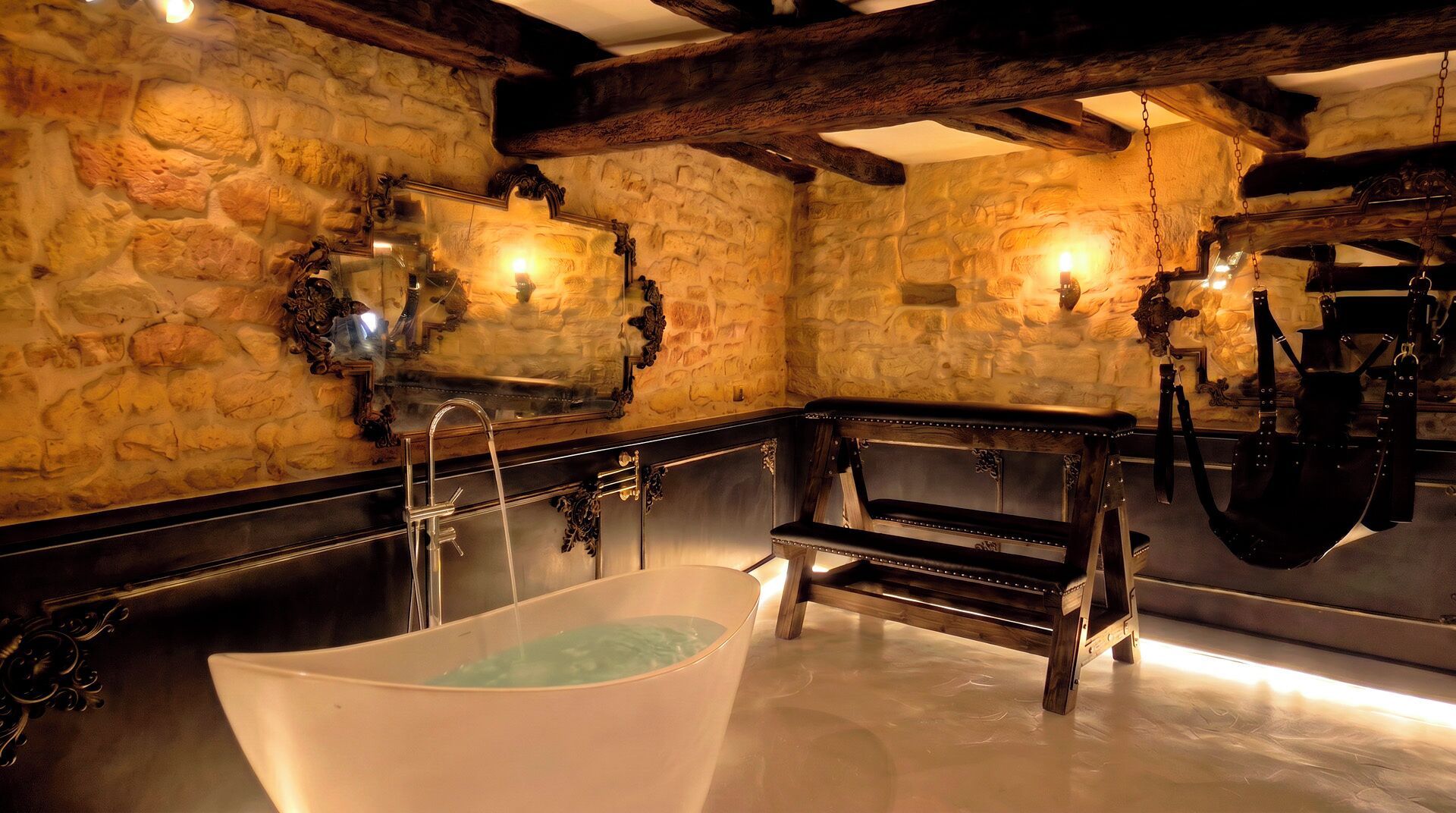 A stone-walled bathroom with a freestanding bathtub, a wooden bench, and a hanging leather strap.
