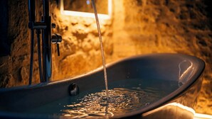 A bathtub with running water, a faucet, and a showerhead in a stone-walled room. - 1503 – Exceptional Suite for Two in the Heart of Historic Sarlat-France (Sarlat la Canéda)