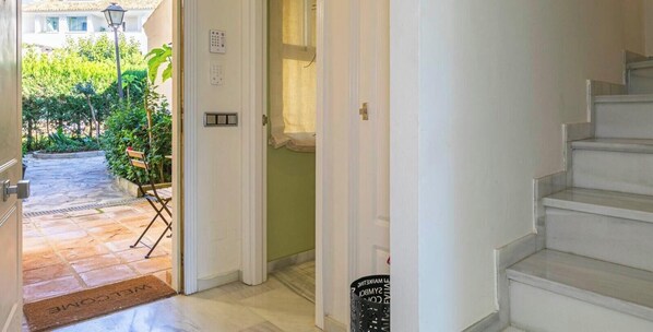 A hotel entrance with a welcome mat, a bench, a door with a light switch, and a staircase. - Holiday Home 'Adosado Puerto Banús Relax' with Private Pool, Wi-Fi and Air Conditioning (Marbella)