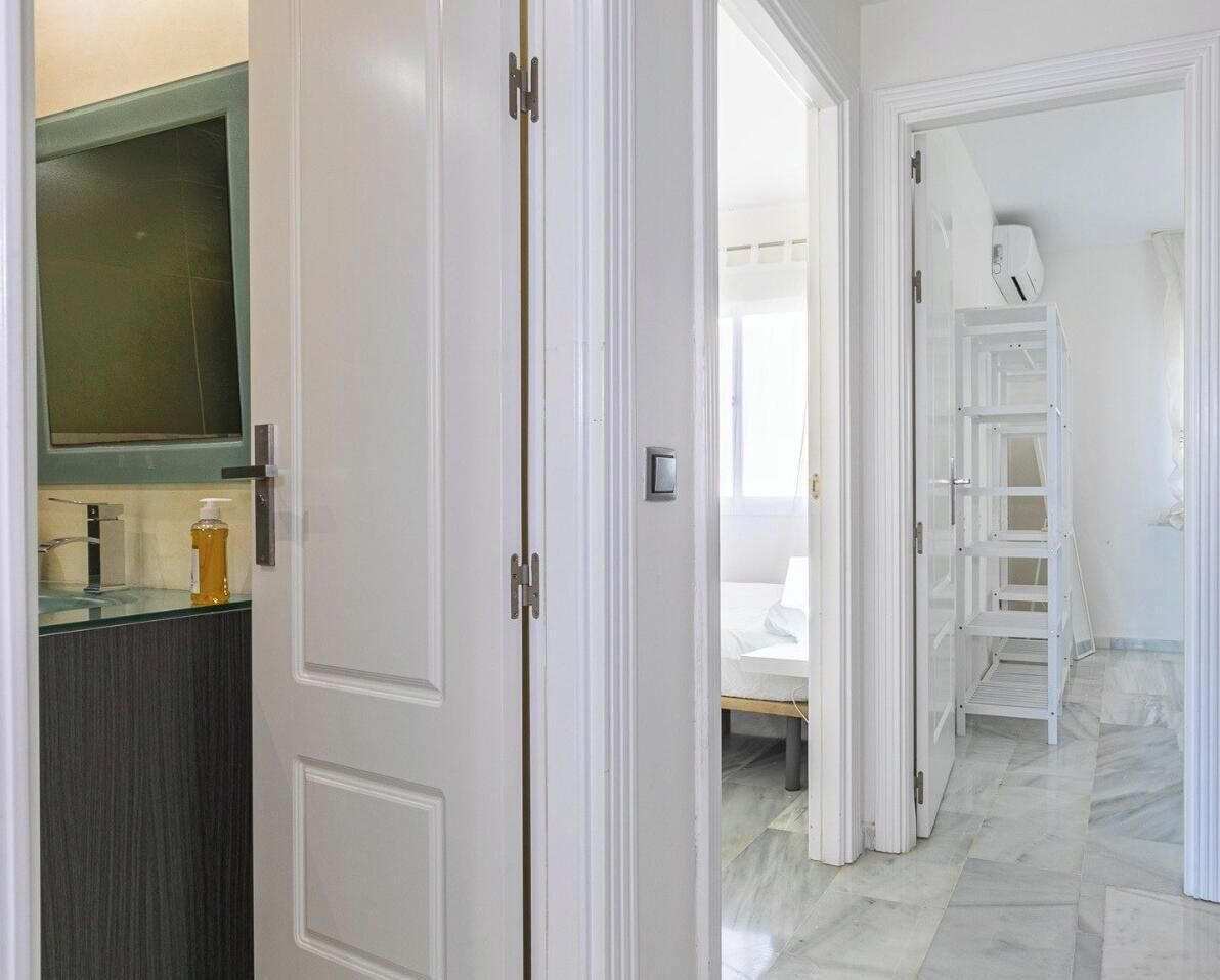 A hotel room with a large bed, a wardrobe, a bathroom with a mirror and sink, and a hallway leading to other rooms.