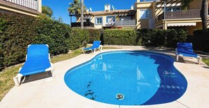 A swimming pool with blue lounge chairs, surrounded by greenery and buildings. - Holiday Home 'Adosado Puerto Banús Relax' with Private Pool, Wi-Fi and Air Conditioning (Marbella)
