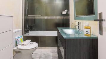 A bathroom with a toilet, a glass shower enclosure, a bathtub, and a vanity with a mirror.