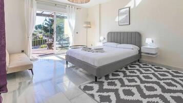 Un dormitorio con cama, mesita de noche, lámpara y una alfombra estampada.