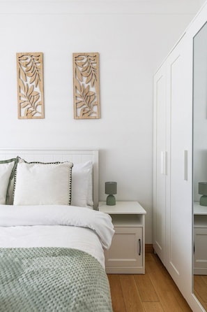 Ein Schlafzimmer mit Bett, Nachttisch, Kleiderschrank und Wandbild.