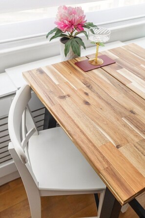 Ein Holztisch mit einem weißen Stuhl, eine Vase mit einer rosa Blume und ein Glas-Kerzenhalter.