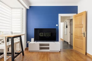 Ein Zimmer mit Fernseher auf einer weißen Unterhaltungsanlage, einer Holztür und einem Fenster mit Jalousien.