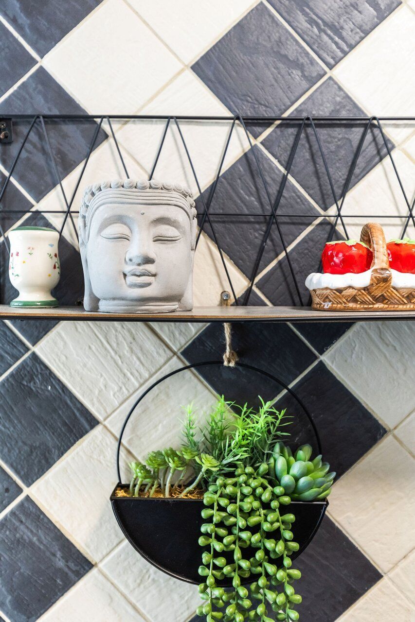 A tiled wall with a geometric pattern, a shelf with decorative items, and a hanging planter with green plants.