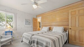 Un dormitorio con dos camas, un escritorio, una silla, un ventilador de techo y un panel de pared de madera.