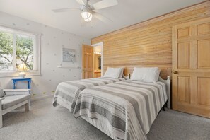 Ein Schlafzimmer mit zwei Betten, einem Schreibtisch, einem Stuhl, einem Deckenventilator und einer Holzwandverkleidung.