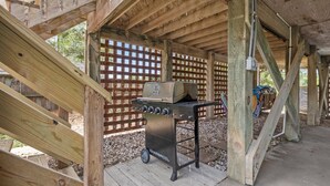Una parrilla de barbacoa debajo de una estructura de madera con un cerramiento de celosía al fondo.