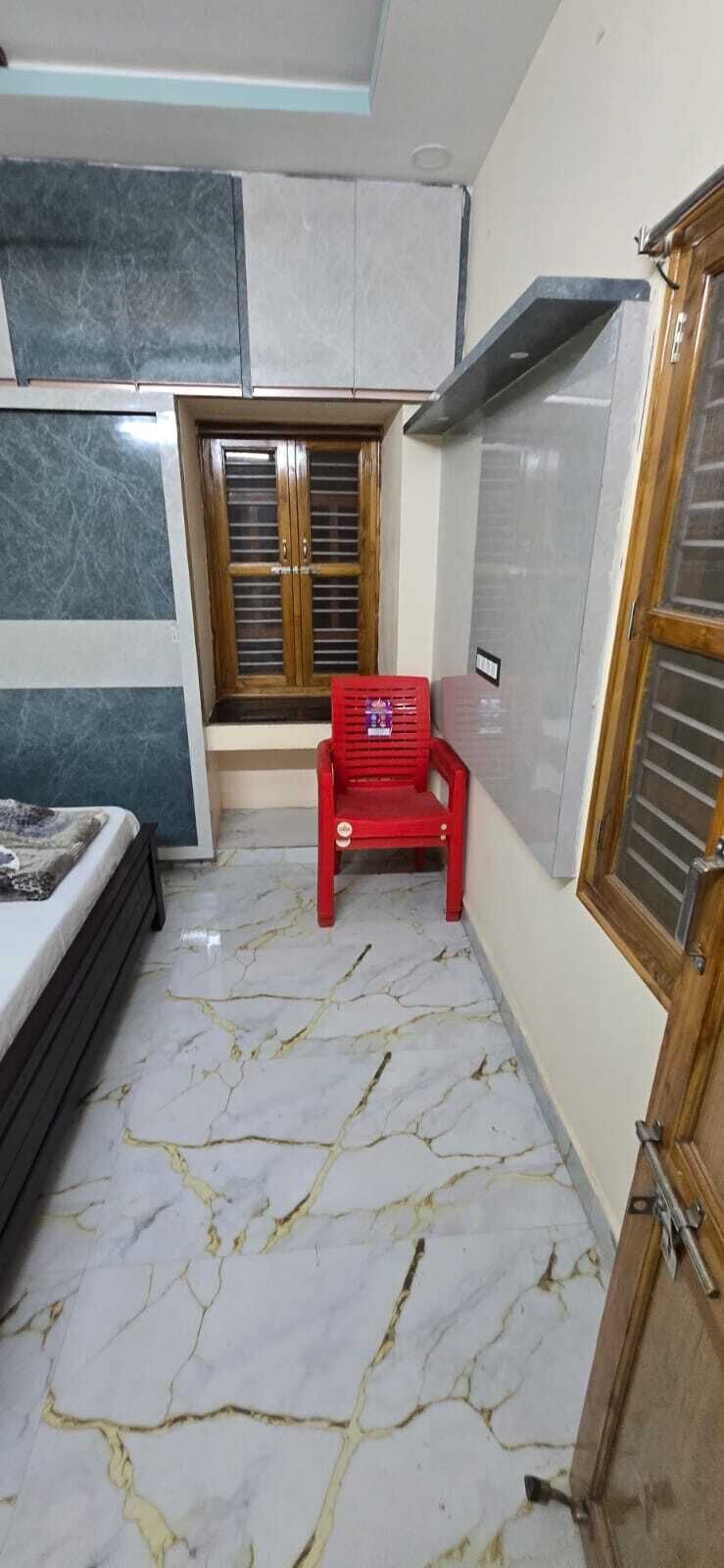 A room with a bed, a window with wooden shutters, a red chair, and a wardrobe.