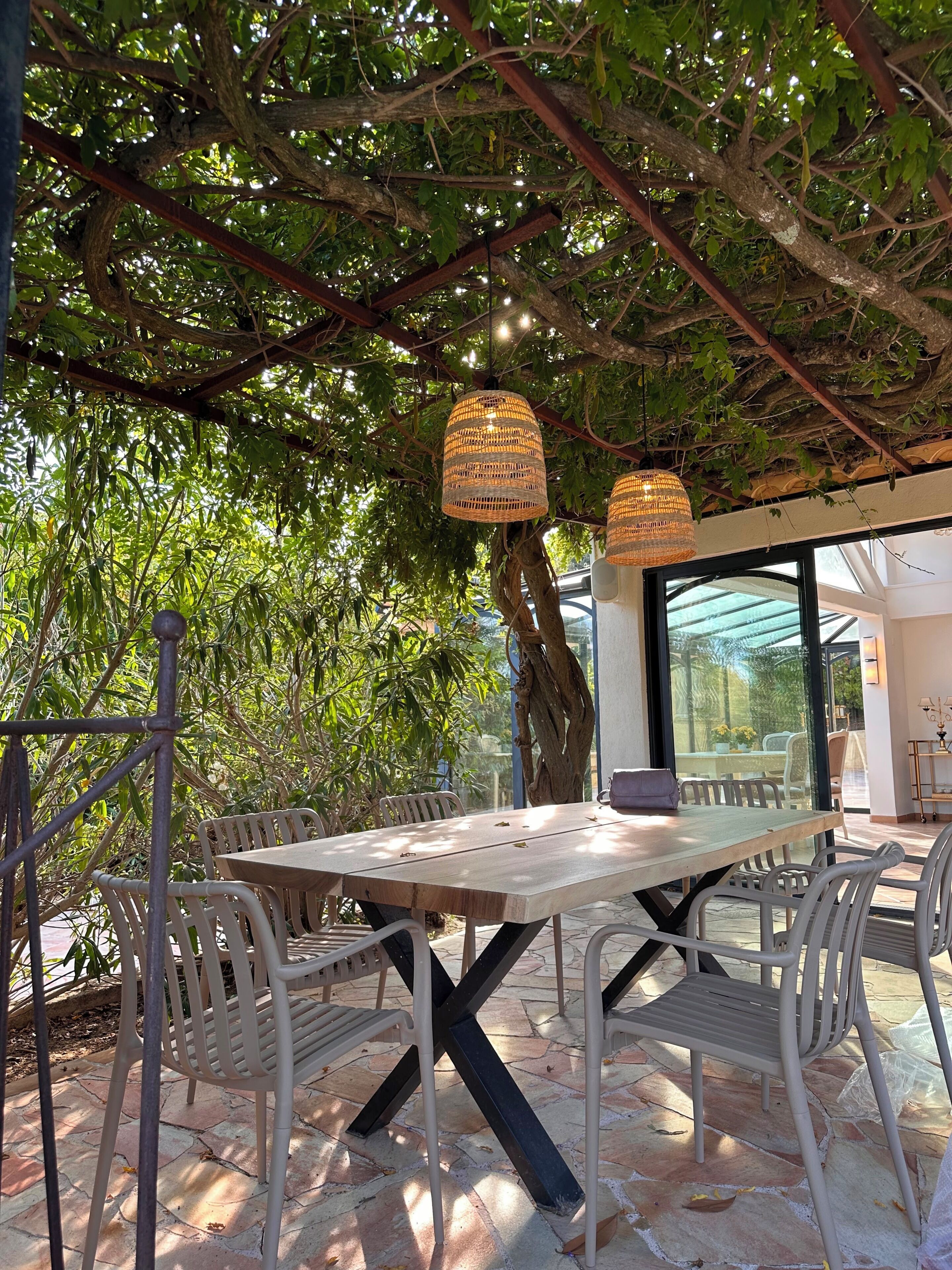 Ein Essbereich im Freien mit Holztisch und Stühlen, umgeben von Pflanzen und einer Pergola.