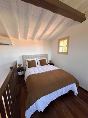 Een slaapkamer met een groot bed, een nachtkastje, een raam en houten balken in het plafond.