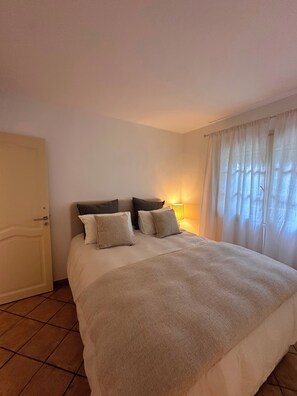 A hotel room with a bed, a bedside lamp, a door, and a window with curtains. - Near Saint Tropez Charming 4 bedroom house swimming pool garden  with AC (La Croix-Valmer)