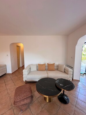Una sala de estar con un sofá, dos mesas redondas y un pequeño reposapiés.