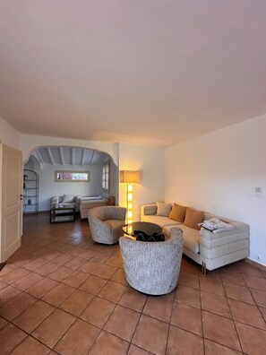 A living room with a sofa, armchairs, a coffee table, and a lamp. There is a door leading to another room. - Near Saint Tropez Charming 4 bedroom house swimming pool garden  with AC (La Croix-Valmer)